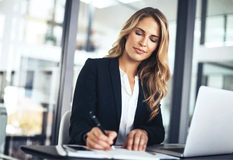 Woman taking notes beside a laptop in an office